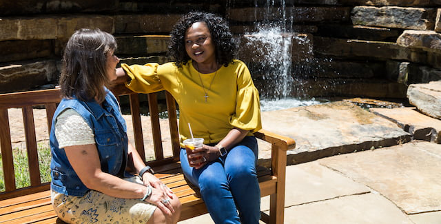 Two women sitting on a bench in front of a waterfall